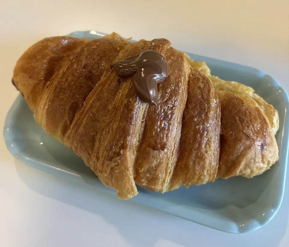 コルネットの実写写真（ヌテッラ入りの現行イタリア風コルネット（バールの朝食様式）。クロワッサン（同祖姉妹#24）と区別するため中身が見えるフィリング入りを選定）