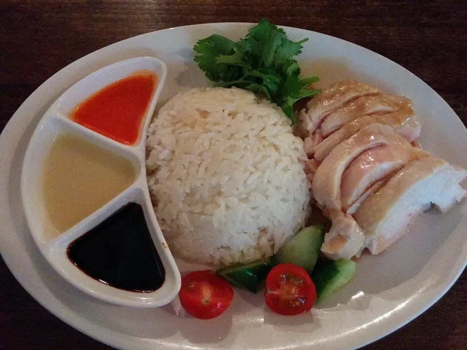 海南鶏飯の実写写真（シンガポール式の代表構図（茹で鶏スライス＋鶏油飯＋三種ダレ皿=チリ/生姜/濃口醤油＋香菜・胡瓜添え）。撮影は東京・六本木のシンガポール料理店だが盛付けは現行シンガポール式の標準形。CC0。）