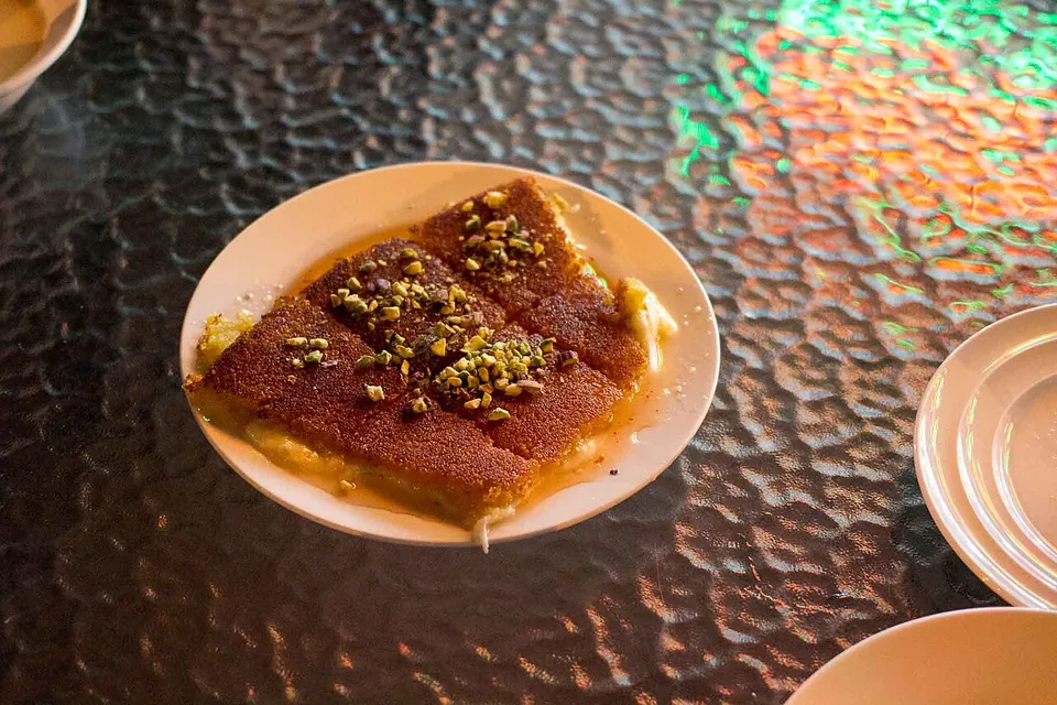 クナーファの実写写真（ナーブルス式クナーファ(kunafa nabulsi/na'ma)＝橙色セモリナ生地+白チーズ層+ピスタチオ。#192のレバント(ナーブルス)現行形に整合）