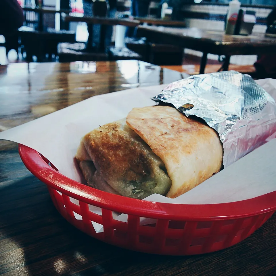 ミッションブリトーの実写写真（サンフランシスコ・ミッション地区のミッションブリトー=La Taqueria(Mission district, SF)の大判アルミ箔巻きブリトー(carnitas・鉄板でトーストしたsuper dorado)。撮影地・店ともミッション式の発祥地に整合=現行形。起源説C）