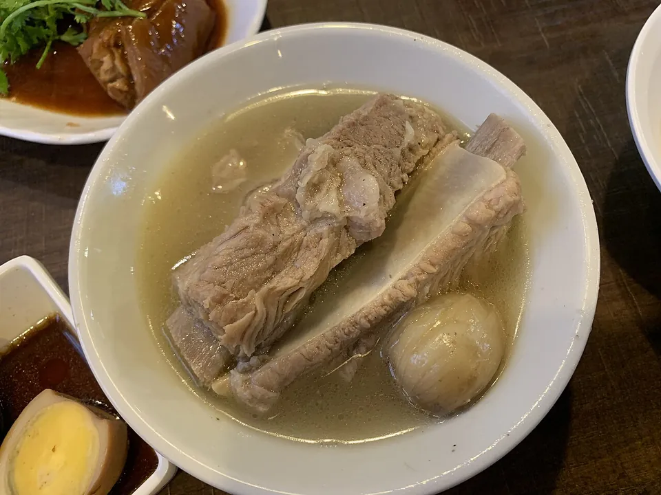バクテー（肉骨茶）の実写写真（シンガポール式バクテー（肉骨茶）の提供直後の完成状態＝骨付き豚リブとニンニクの澄んだ胡椒スープ椀、煮卵・タレ小皿を添える。撮影はシンガポール Song Fa Bak Kut Teh（当料理の代表店）で origin 整合。↺再挑戦=前回却下『食べかけ』を回避（未着手の一椀）。CC BY 4.0=帰属付き。）