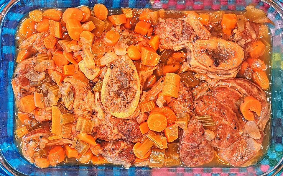 オッソブーコの実写写真（現行形の完成皿。仔牛すね肉の骨付き蒸し煮に人参・セロリを添えた明るい一枚（前回却下#106『画像が暗い』の是正）。ミラノ式の定番サフランリゾット添えではないが、オッソブーコ本体（骨髄を残す骨付きすね肉の煮込み）を明快に示す。）