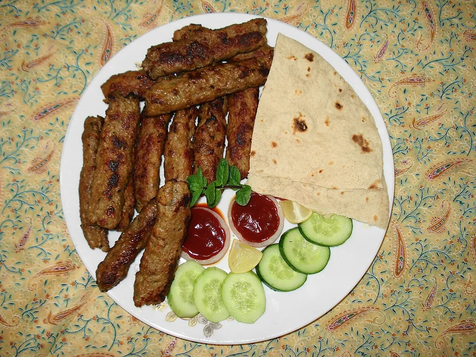 シークカバブの実写写真（現行形の完成皿。串成形した挽き肉(羊/牛)を炭火で焼いたシークカバブ。円盤状のシャミ/チャプリカバブとは別物。ロティ・薬味添え。パキスタン/パンジャーブ料理でラホール地域整合。）